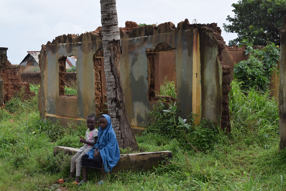 Two girls sitting in front of a destroyed building in Kasuwan Magani