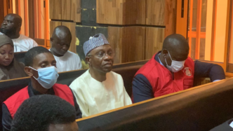 Godwin Emefiele (in white) flanked by two EFCC operatives, in court | File photo